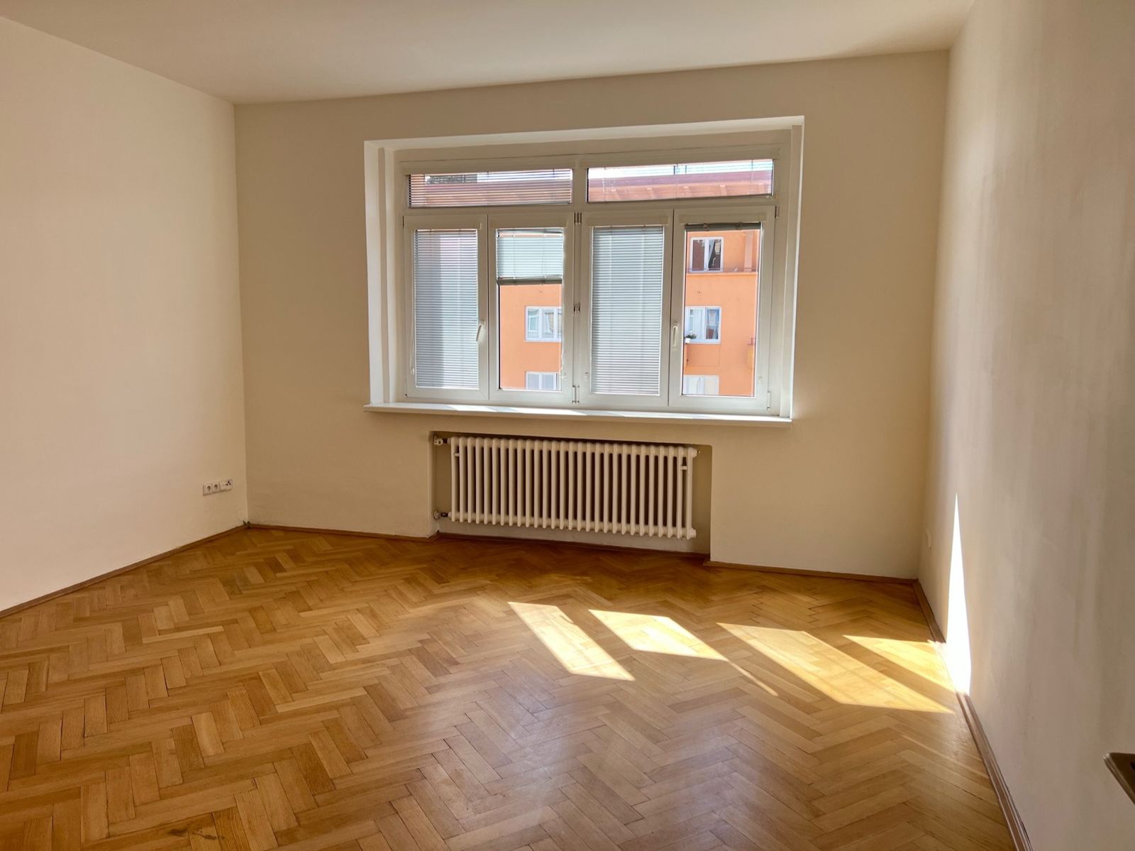 Světlý pokoj s parketami ve vzoru rybí kosti a velkým oknem